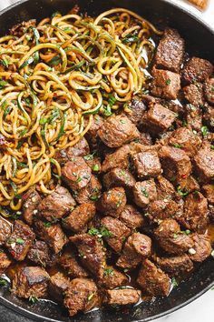 meat and noodles in a skillet on a white surface with chopsticks next to it