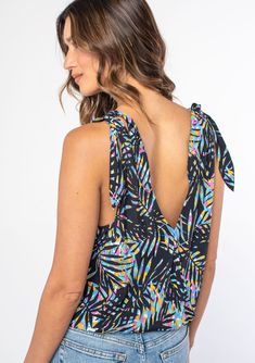 [Color: Black/Blue] A woman wearing a black sleeveless tank top with a blue tropical palm print and a tie shoulder accent. V-neck Tie Back Tank Top For Beach, Beachwear V-neck Tops With Tropical Print, V-neck Floral Print Tank Top For Beach, Vacation V-neck Tank Top With Tie Back, V-neck Tank Top With Tie Back For Beach, Adjustable Straps Sleeveless Tank Top For Beachwear, Sleeveless Palm Tree Print Swimwear For Summer, Beach Season Tie Back Tops, Vacation V-neck Top With Tie Straps