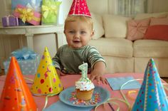 a baby sitting at a table with a cupcake and birthday hats on it's head