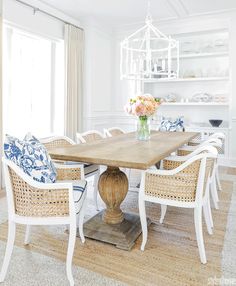 a dining room table with wicker chairs around it and flowers in vase on top