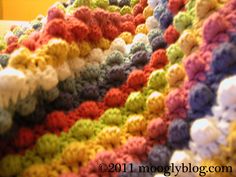 a multicolored crocheted blanket is laying on the floor next to a wall