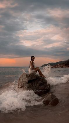 a woman sitting on top of a rock in the ocean next to an ocean shore