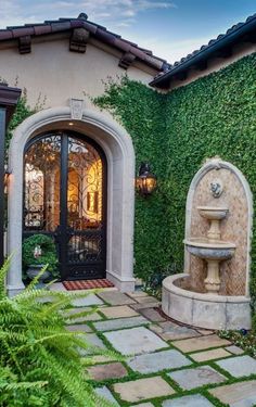 the entrance to a home with a fountain in front of it and green plants growing on the wall