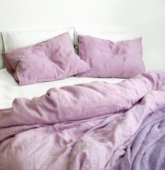 an unmade bed with purple sheets and pillows