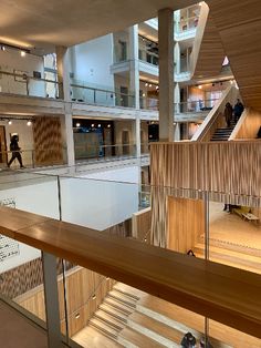 people are walking up and down the stairs in a large building with wooden walls, glass balconies, and metal railings