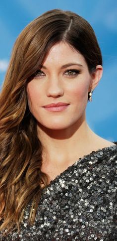 a woman with long brown hair wearing a black and silver dress, smiling at the camera