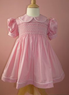 A beautiful hand smocked party dress in a baby pink thick Japanese cotton sateen. Delicately hand smocked with a geometric design on the front and tied with a large bow and mother of pearl buttons in the back. Fully lined in 100% cotton. Each dress is made to order so can be customised to your wishes, please leave a note at checkout or send me a message to discuss. Please allow up to two weeks for dispatch. Elegant Smocked Dress With Smocked Cuffs For Baptism, Elegant Pink Dress With Smocked Cuffs, Pink Fitted Smocked Dress With Short Sleeves, Pink Fitted Dress With Smocked Cuffs, Elegant Pink Dress With Smocked Back, Pink Cotton Smocked Dress With Short Sleeves, Elegant Cotton Smocked Dress With Smocked Cuffs, Pink Cotton Smock Dress, Pink Smock Cotton Dress