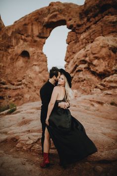 a man and woman are standing in front of some rocks, one is wearing a black dress