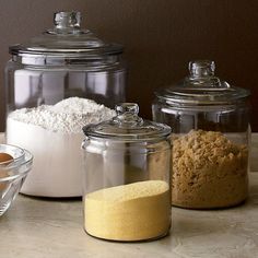 three glass containers filled with food on top of a counter next to bowls and spoons