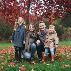 a family posing for a photo in front of a tree with red leaves on it