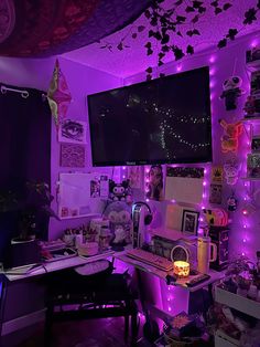 a room with purple lighting and lots of clutter on the desk, in front of a flat screen tv