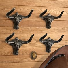 four metal steer head hooks hang on a wooden wall next to a pair of cowboy boots