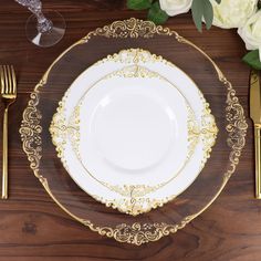 a white plate with gold trim on top of a wooden table next to silverware and flowers