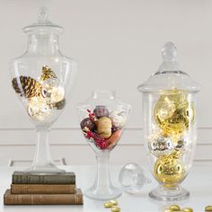 three glass vases filled with different types of ornaments on top of a white table