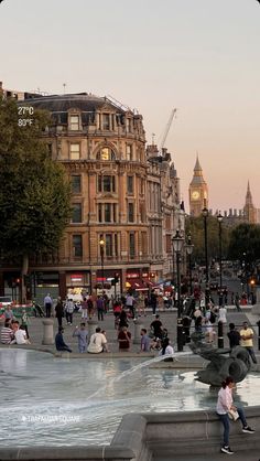 people are sitting and walking around in the city square at sunset or dawn, with big ben in the background