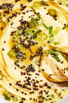 a white bowl filled with food covered in cheese and black seeds next to a spoon