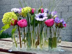 a bunch of flowers are in vases on a wooden table with grass and water