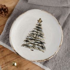 a white plate with a christmas tree painted on it and two gold bells next to it