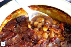 a bowl filled with beans and meat on top of a white plate next to a spoon