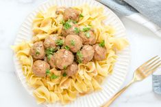 a white plate topped with meatballs and pasta on top of a marble countertop