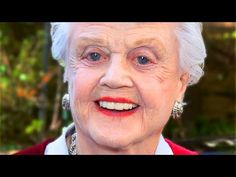 an older woman with white hair and earrings smiling at the camera while standing in front of a car