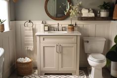 a white toilet sitting next to a sink in a bathroom under a large round mirror