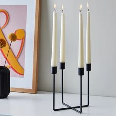 three white candles sitting on top of a table next to a vase with flowers in it