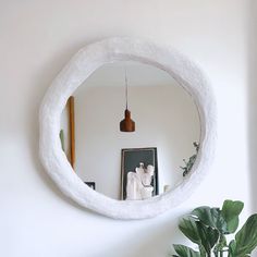 a mirror hanging on the wall above a potted plant and a white horse statue