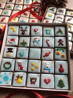 a box filled with lots of decorated cookies on top of a wooden table next to pine cones