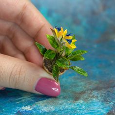 a woman's hand holding a tiny plant with yellow flowers