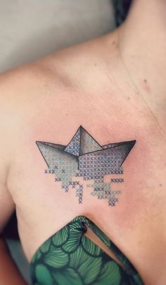 a woman's chest with an origami paper boat tattoo on her left shoulder