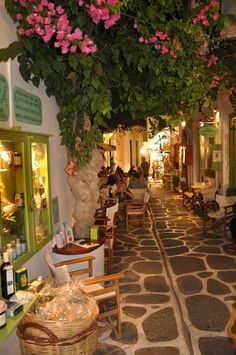 an alley way with tables and chairs lined up along the wall, covered in pink flowers