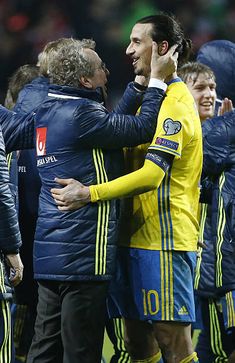 two soccer players are hugging each other on the field while others look on and smile