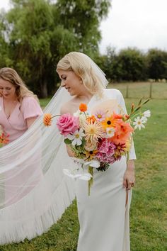 two women in wedding dresses are walking through the grass with their veil flying over them