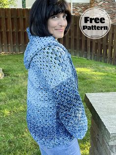 a woman standing in front of a brick wall wearing a blue crochet sweater