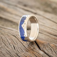 a wedding ring with blue and white stone inlayed to the side on a wooden surface