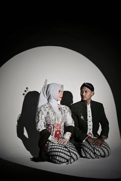 a man and woman sitting on the ground in front of a white wall with shadows