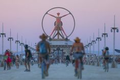 many people are walking and riding bikes in front of a large structure with a man on it