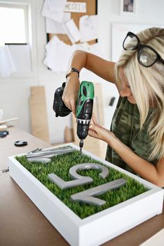 a woman is using a drill to cut grass in the shape of a letter on a table