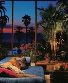 a living room filled with lots of furniture next to tall windows overlooking the ocean and palm trees