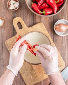 a person in white gloves is cutting red peppers on a wooden table with other ingredients