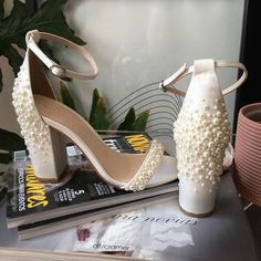 a pair of white high heeled shoes sitting on top of a book next to a plant