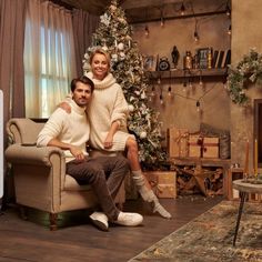 a man and woman sitting in front of a christmas tree