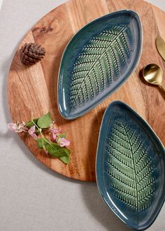 two blue plates with green leaves on them and gold spoons next to each other