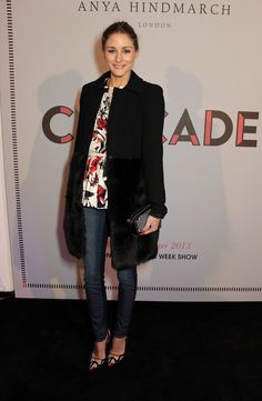 a woman standing in front of a wall wearing a black jacket and floral shirt with fur collar