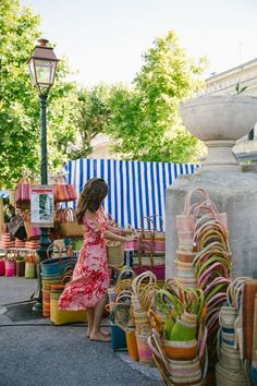 a woman in a red and white dress is looking at baskets on the ground near a lamp post