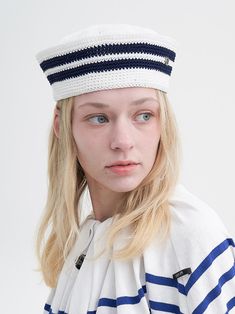 a woman with blonde hair wearing a sailor's cap and striped shirt, looking at the camera