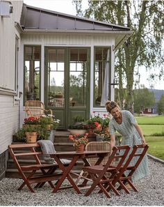 a woman standing in front of a house next to a table with chairs on it