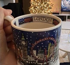 a hand holding a coffee cup with the london skyline on it and a christmas tree in the background