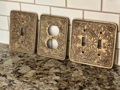 three decorative switch plates on a marble countertop next to a white tile backsplash